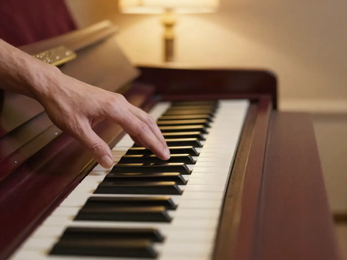 Close-up of a left hand pressing a three-note chord on ivory keys